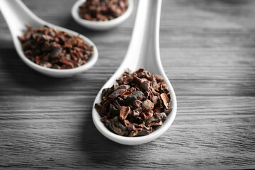 White spoons with cocoa nibs on wooden table