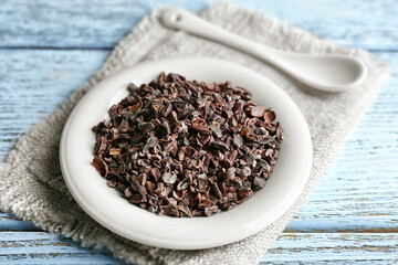 Plate with cocoa nibs on wooden table