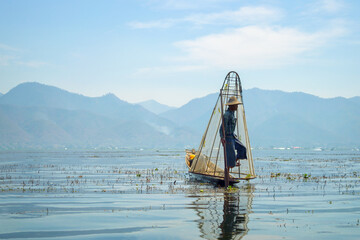 Burmese fisherman on bamboo boat catching fish in traditional way with handmade net. Inle lake, Myanmar (Burma), travel destination
