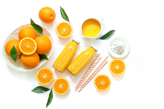 Two glass bottles of fresh orange juice, straws and oranges isolated on white background top view.