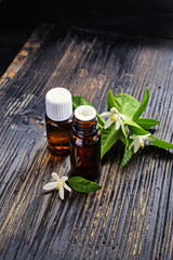 Neroli (Citrus aurantium) essential oil in a brown glass bottle with fresh white flowers on old black textured wooden background. Copy space, Selective focus.