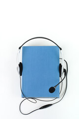 Audiobook on white background. Headphones put over blue hardback book, empty cover, copy space for ad text. Distance education, e-learning concept.