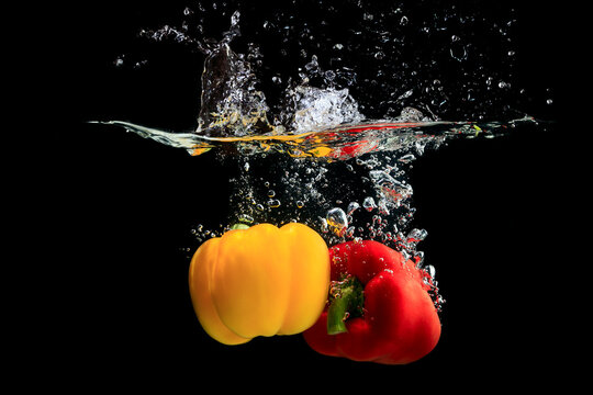 Yellow and red pepper splashing water on black background