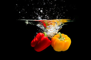 Yellow and red pepper splashing water on black background