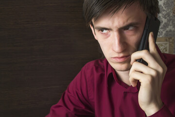 A young man in a purple shirt is waiting for an answer on a black smartphone, with an alarming suspicious look, frowning