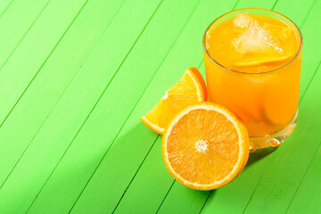 A glass of orange juice with ice on green wooden table