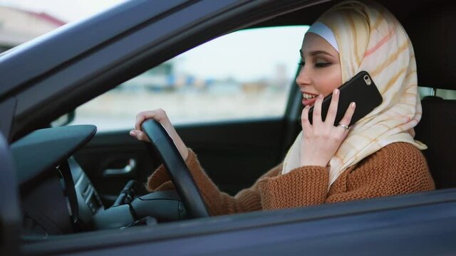 Young Muslim woman wearing a headscarf having a phone talk sitting in the drivers seat. Day-to-day life of modern Muslim women