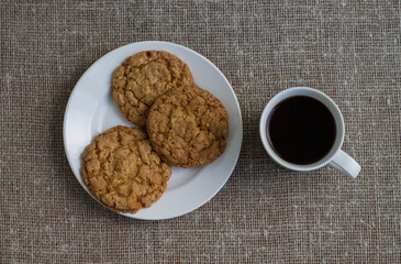 Cookies on a white plate and mug with coffee. Background of burlap