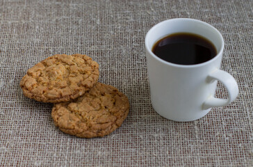 Cookies on a white plate and mug with coffee. Background of burlap