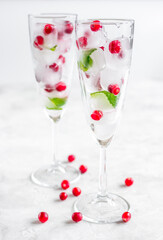 ice cubes with red berries and mint in glasses on white background