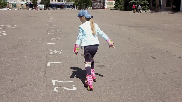 Little girl learning to roller skate in sunny summer park. Child wearing protection elbow and knee pads, wrist guards for safe roller skating ride. Active outdoor sport for kids.