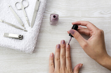 Female hands applying purple nail polish on wooden table with towel and nail set