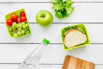 homemade lunch with apple, grape and sandwich in green lunchbox top view