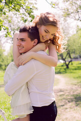 Fototapeta premium bride and groom with a bouquet of red peonies in the summer standing in a field with blooming apple trees