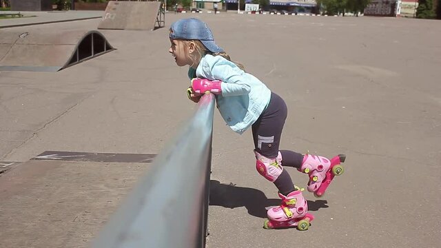 Little girl learning to roller skate in sunny summer park. Child wearing protection elbow and knee pads, wrist guards for safe roller skating ride. Active outdoor sport for kids.