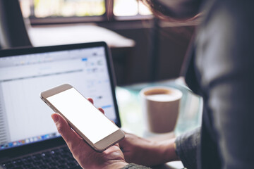 Mockup image of business woman holding mobile phone with blank white screen with latop on wooden table in cafe