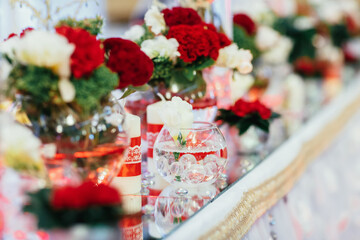 Red bouquets with greenery stand on mirror trays on dinner table