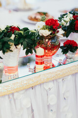 Red bouquets with greenery stand on mirror trays on dinner table