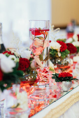 Red bouquets with greenery stand on mirror trays on dinner table