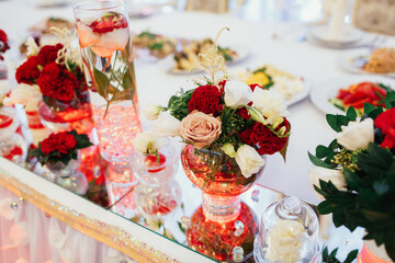 Red bouquets with greenery stand on mirror trays on dinner table