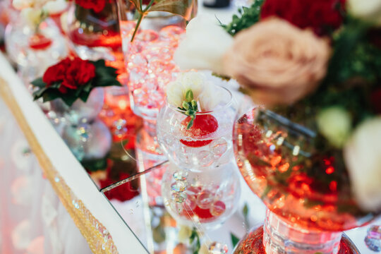 Red bouquets with greenery stand on mirror trays on dinner table