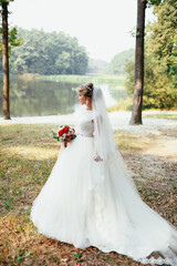 Bride poses with red wedding bouquet on the shore of a lake