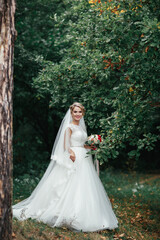 Bride with red wedding bouquet stands before a sick tree