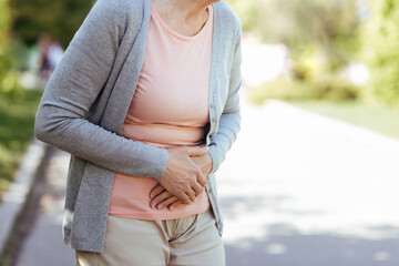 Upset old woman having sudden pain in the stomach outdoors