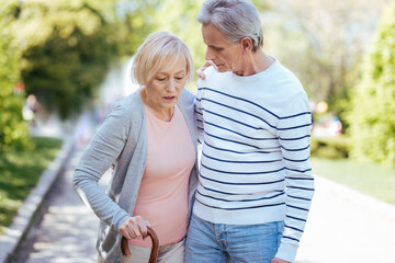 Aging man supporting ill wife in the park
