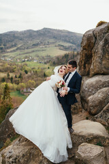 Wedding couple has fun posing on the rocks with great landscape behind