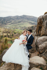 Wedding couple has fun posing on the rocks with great landscape behind