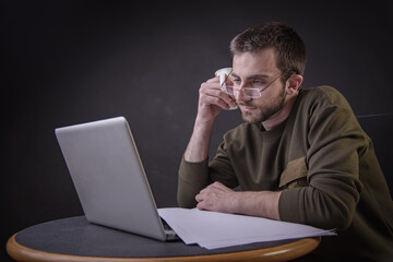 Young man enjoying his coffee and working on laptop, freelance writer or a blogger