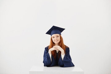 Beautiful ginger graduate smiling looking at camera sitting over white background.