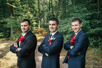 Groom and groomsmen stand in the row posing in the forest