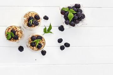 Naklejka na ściany i meble Blackberry parfaits made with Greek yogurt, granola and fresh blackberries shot from overhead over white wood table. Room for copy space.