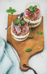 Healthy breakfast. Greek yogurt, granola, blood orange layered parfait in glasses with fresh mint leaves on rustic wooden board over grey marble background. Clean eating, weight loss food concept