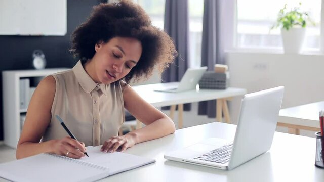 young businesswoman working in modern office sitting at the table with laptop and taking notes