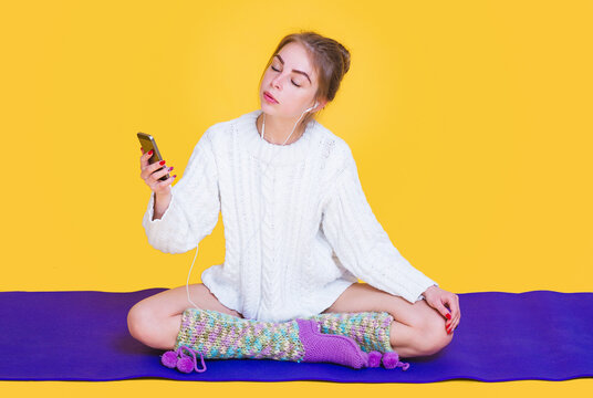 Beautiful young yogini woman sitting down in lotus pose on purple mat and listening to relaxing music from her phone