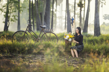 Beautiful Asian woman in local traditional dress with old bicycle and flower basket on the green summer field.