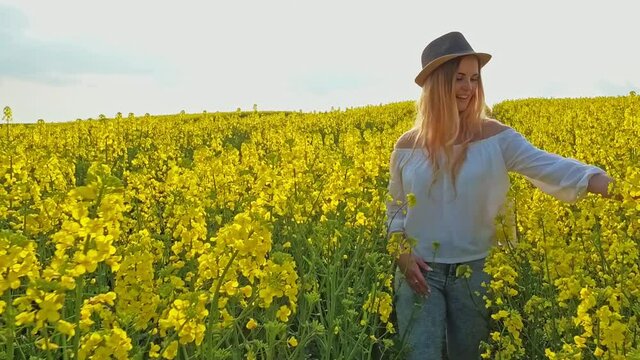 Happy woman with long hair walks on yellow field touching flowers, slow motion