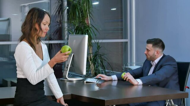 Two office workers having a break, aeting green apples and talking in office