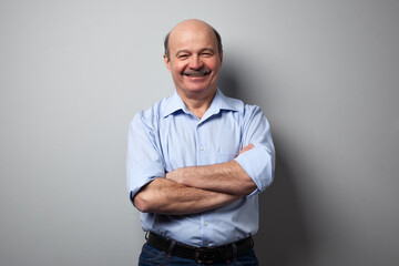 A man with a mustache stands against the wall, arms crossed over his chest