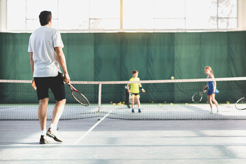 Male coach playing tennis with kids