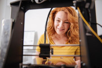 Fototapeta na wymiar Cheerful delighted woman observing a 3d printer in work