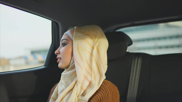 Happy muslim woman in a car on a passenger rear seat. She looking at the window