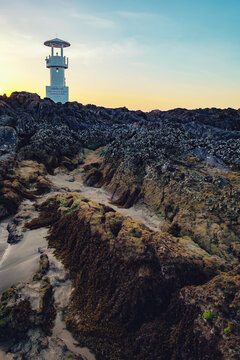 Lighthouse in the evening twilight, Nang Thong Beach, Khao Lak, Thailand. Stones covered with seaweed in the foreground