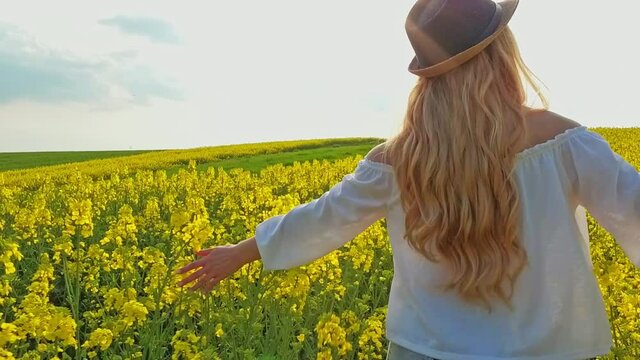 Happy woman with long hair running on yellow field touching flowers