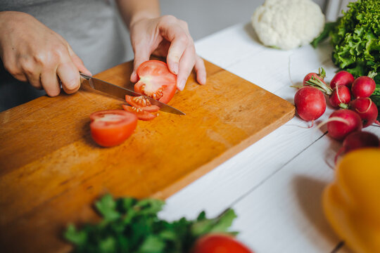 Woman hands cutting fresh red tomato on wooden board closeup. White table background.