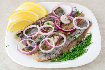 Marinated herring fillets with red onion, dill and spices on white plate.