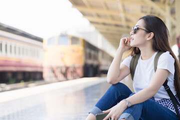 Young asian cute woman is sitting on the floor and smiling at platform train station. Travel summer concept.